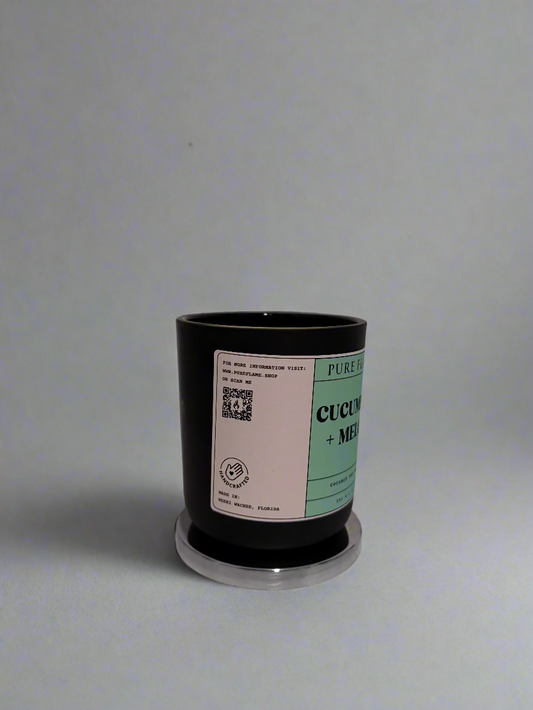 Black candle with a label on a white surface against a white wall